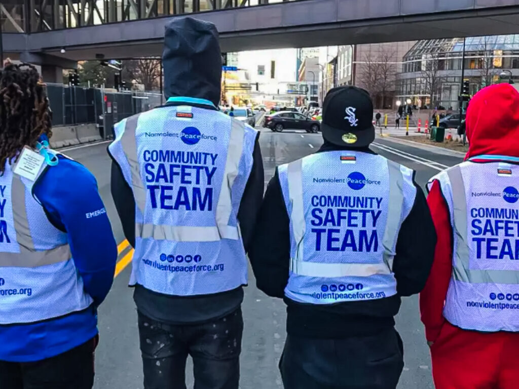 Das Titelbild zeigt vier Mitglieder des Community Safety Teams („Ziviles Schutzteam“) der Nonviolent Peaceforce in Minnesota, USA.