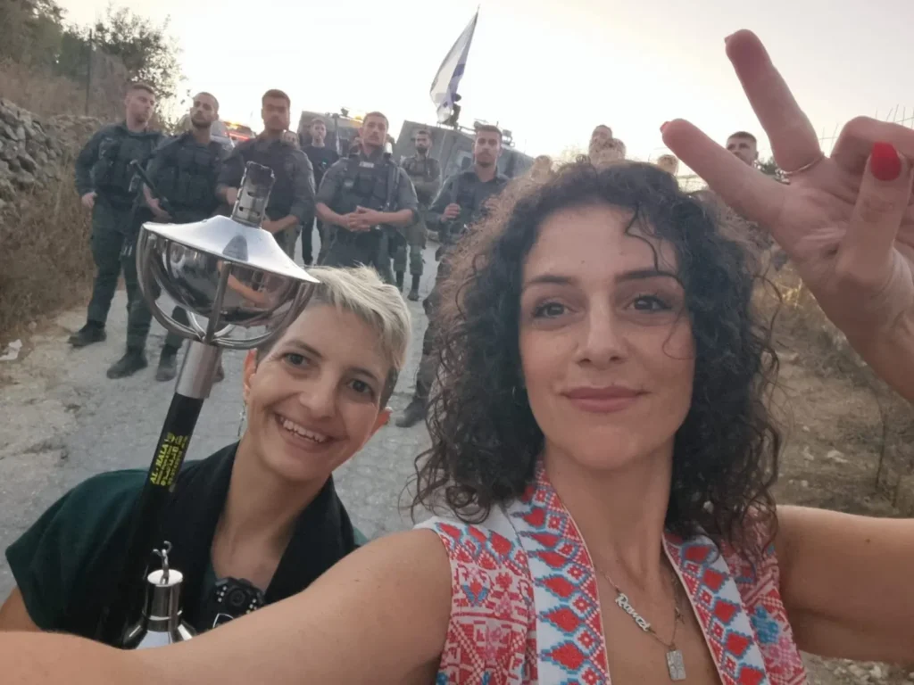 Hier ist das Titelbild zu sehen. Es zeigt zuversichtliche Mitglieder der Combatants for Peace, Amira Musallam (rechts), die das Friedenszeichen zeigt, und Mai Shahin (links) vor israelischen Soldaten, die ihnen den Weg versperren.