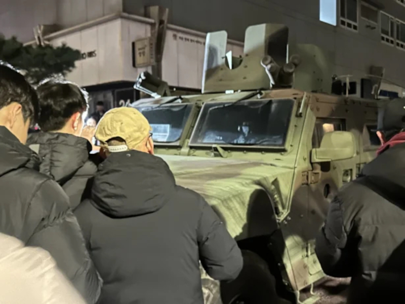 Hier ist Bild 1 zu sehen. Es zeigt südkoreanische Bürger*innen, die ein gepanzertes Fahrzeug der Putschisten blockieren