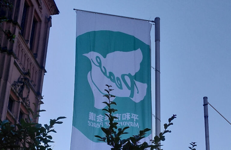 Das Titelbild zeigt die Mayors-for-Peace-Flagge neben dem Alten Rathaus von Weinheim